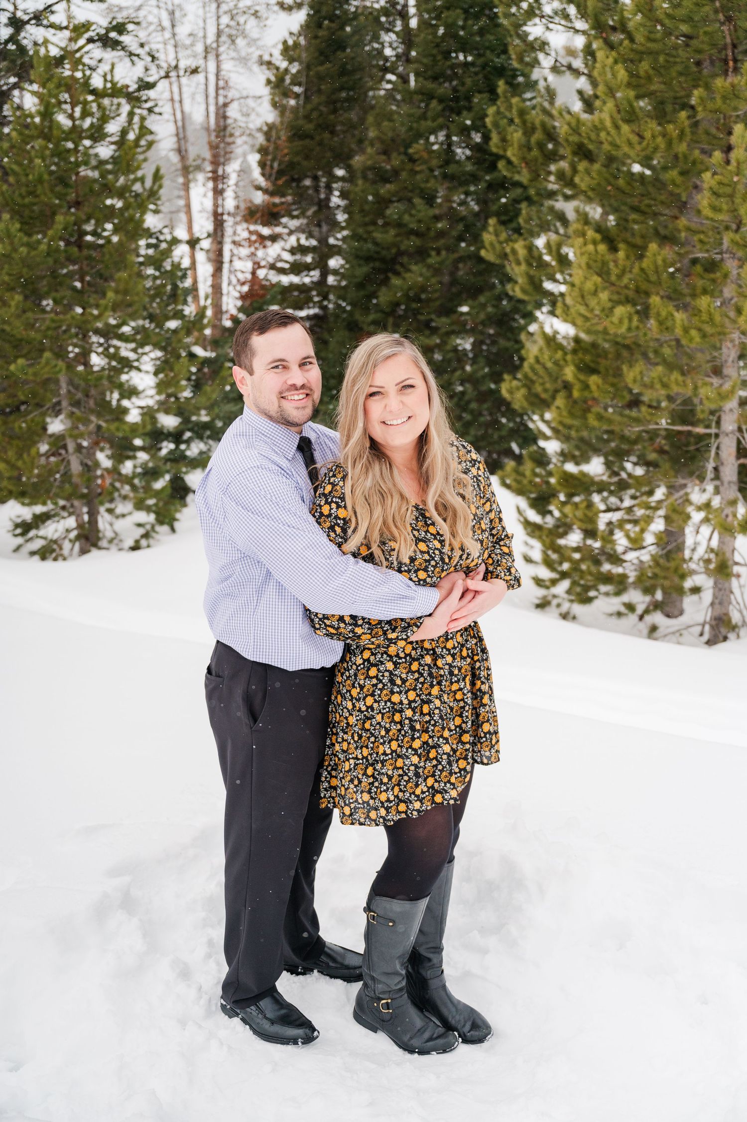 A couple posing together in winter attire against a snowy mountain landscape.