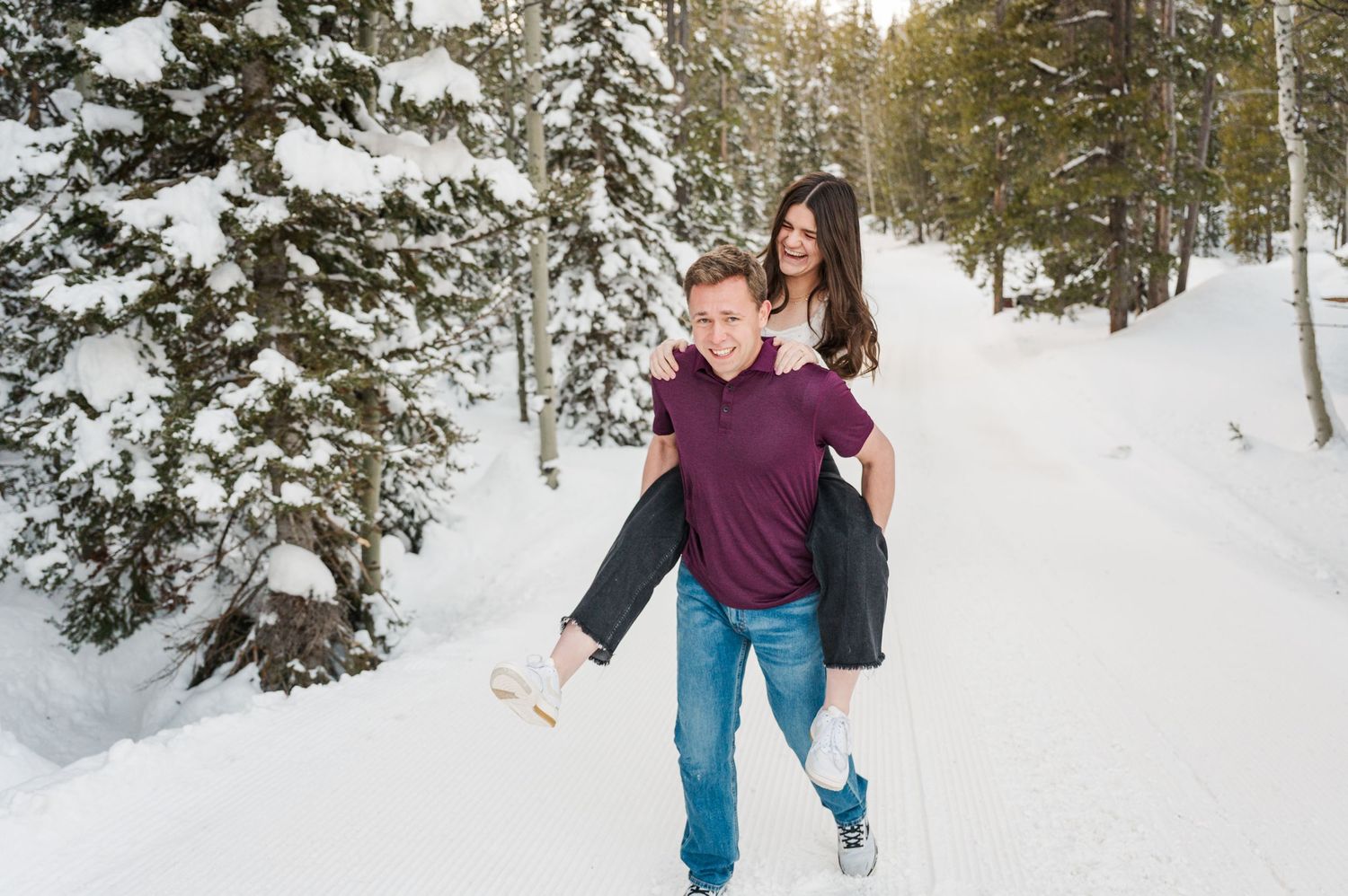 A couple enjoying a playful piggyback ride in a snowy winter forest setting.