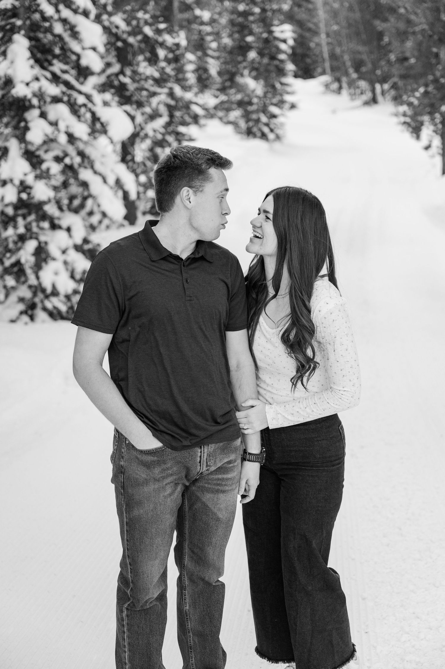 Black and white portrait of couple sharing intimate moment in snowy forest setting.