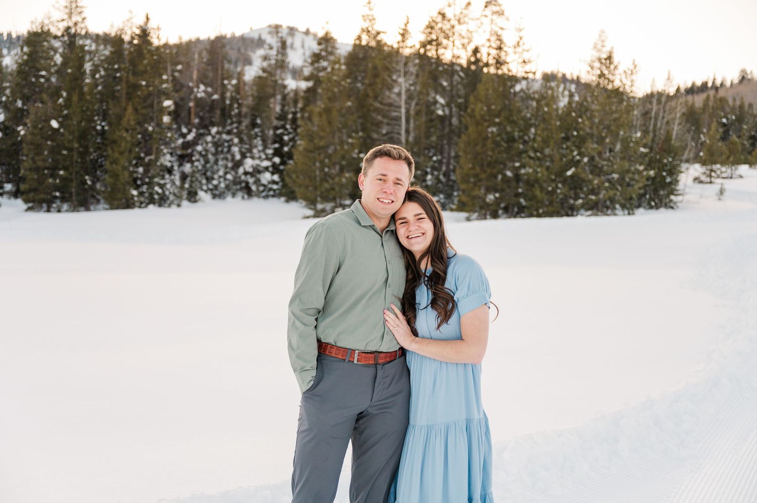 Happy couple poses together in snowy mountain setting wearing coordinated winter outfits.