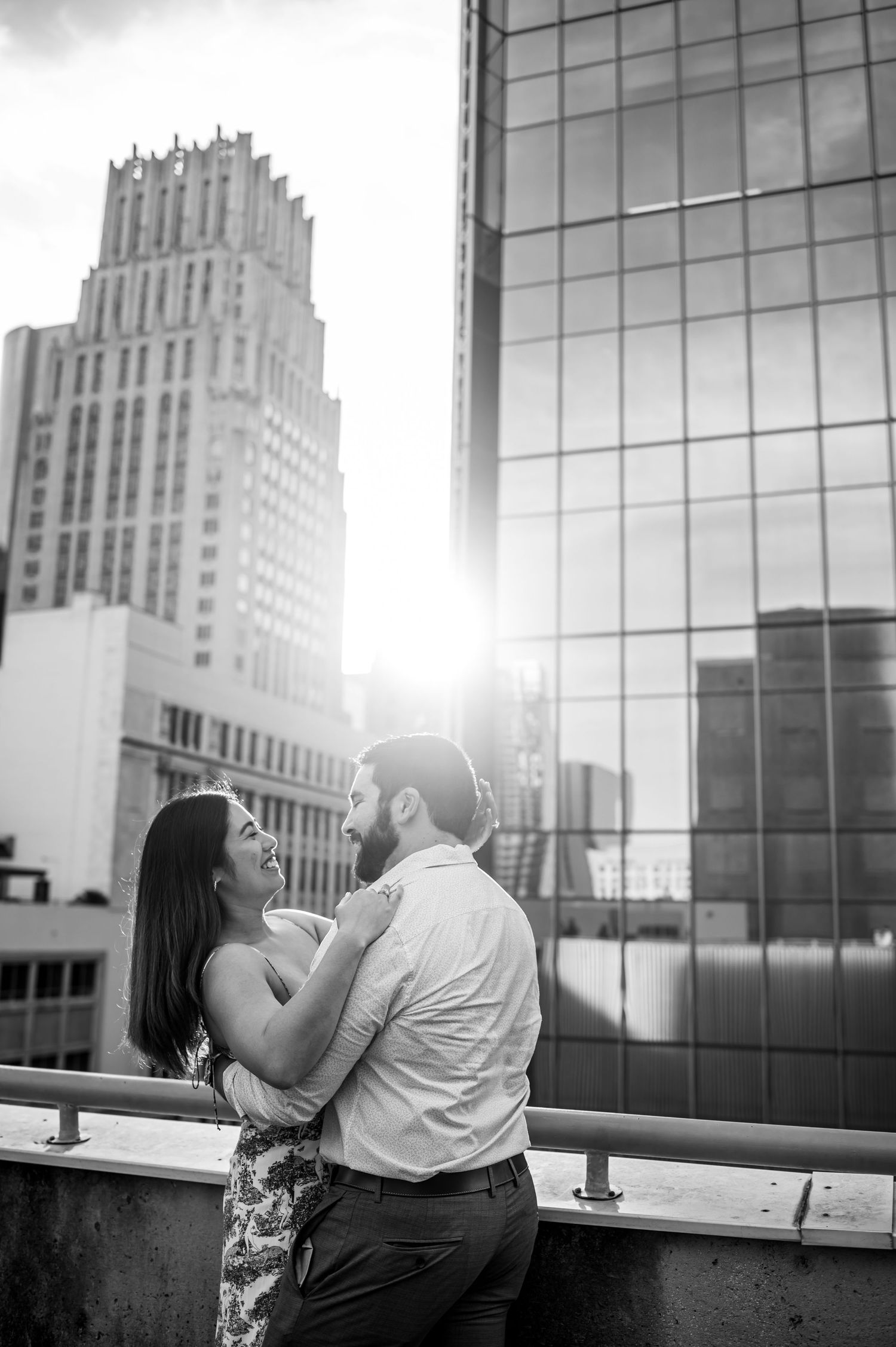 A romantic couple embraces on a rooftop with an art deco building in the background.