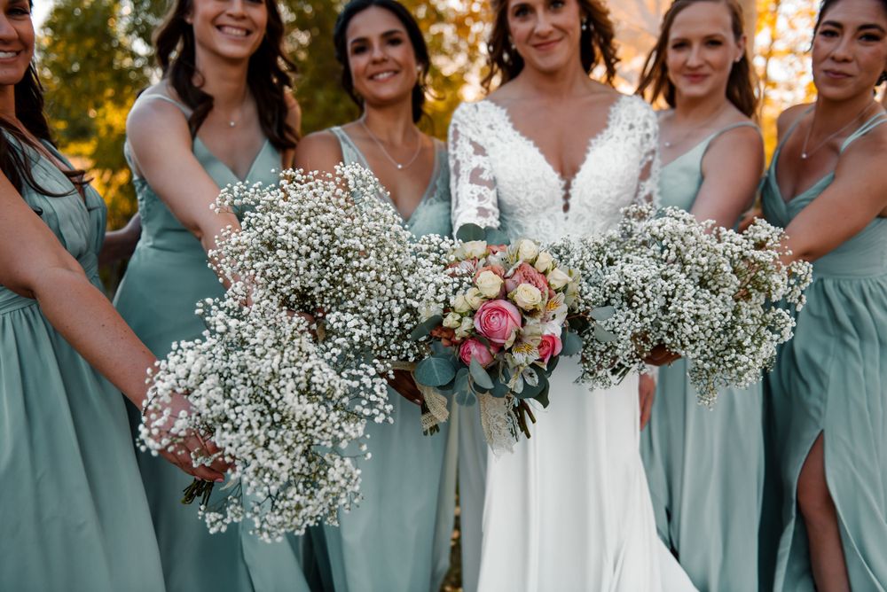 Wedding party in sage green dresses holding baby's breath bouquets.
