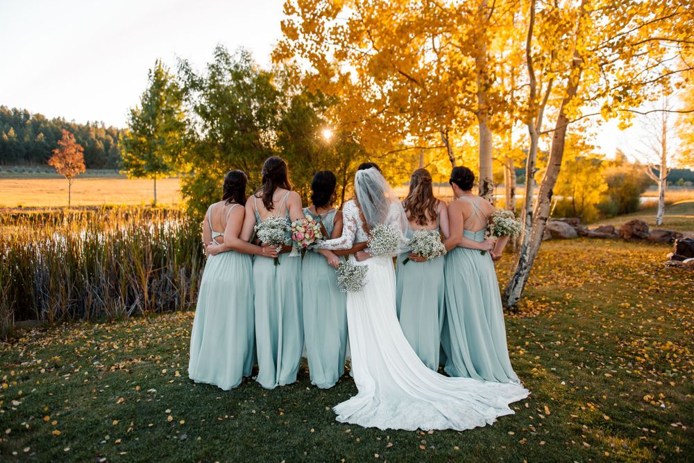 Wedding group photo with bridesmaids in mint dresses surrounded by fall foliage.