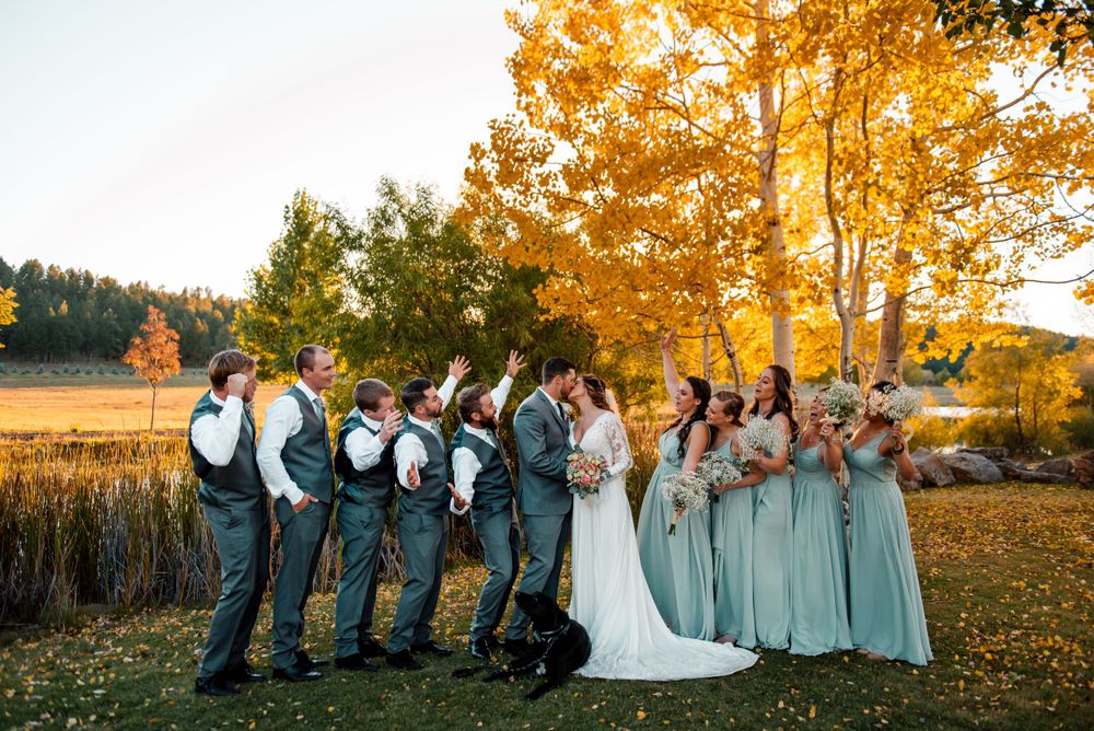Wedding party group shot with bridesmaids and groomsmen in front of autumn trees.