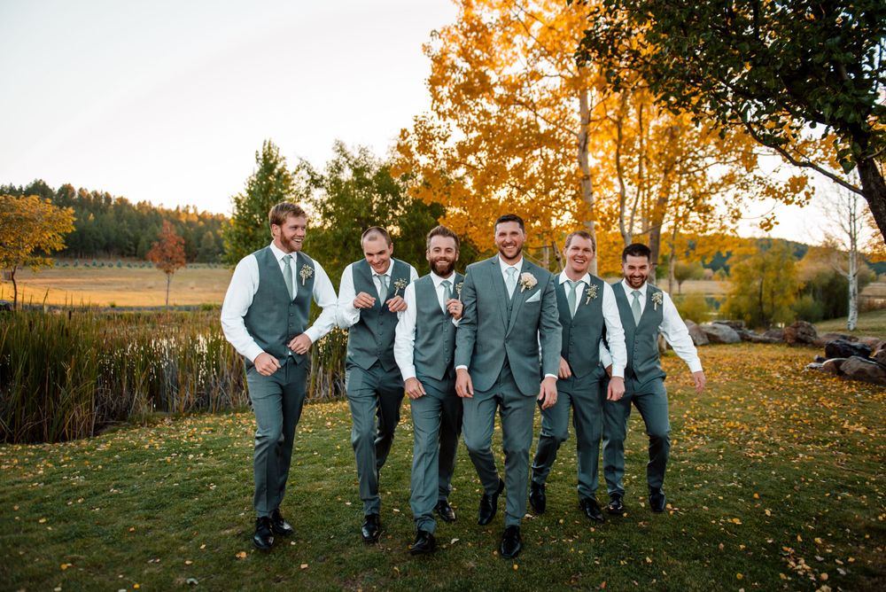 Groomsmen in matching gray vests and suits walk together on grass during golden hour.