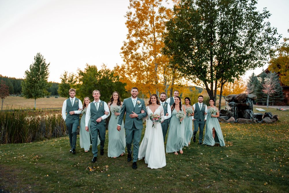 A wedding party celebrates on a lawn with autumn trees in the background.