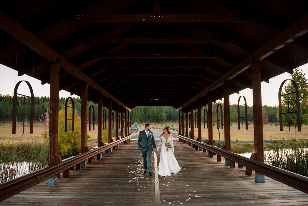 Couple in wedding attire poses romantically in a rustic covered wooden walkway with dramatic lighting.