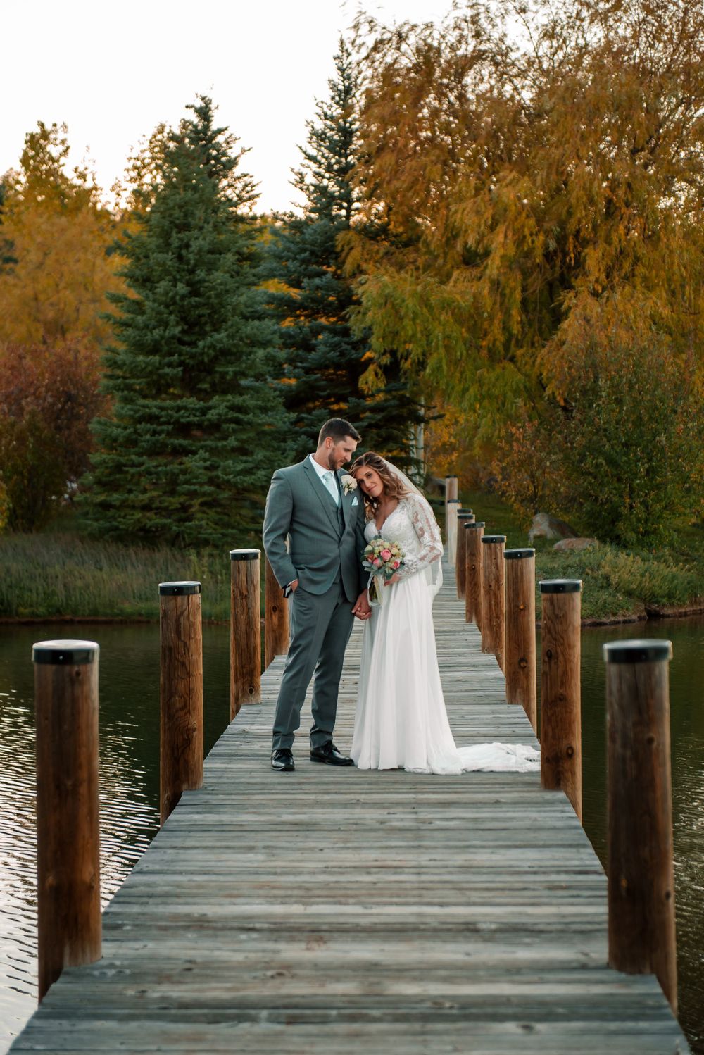 Newlyweds share intimate moments on a lakeside dock surrounded by autumn trees.