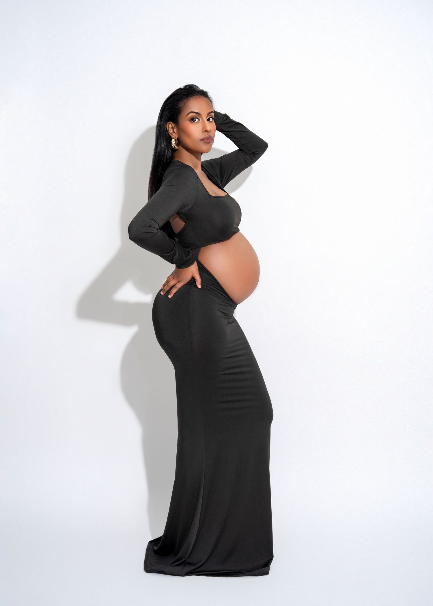 studio maternity photo shoot a woman stands in front of a white backdrop with her back arched in an editorial style