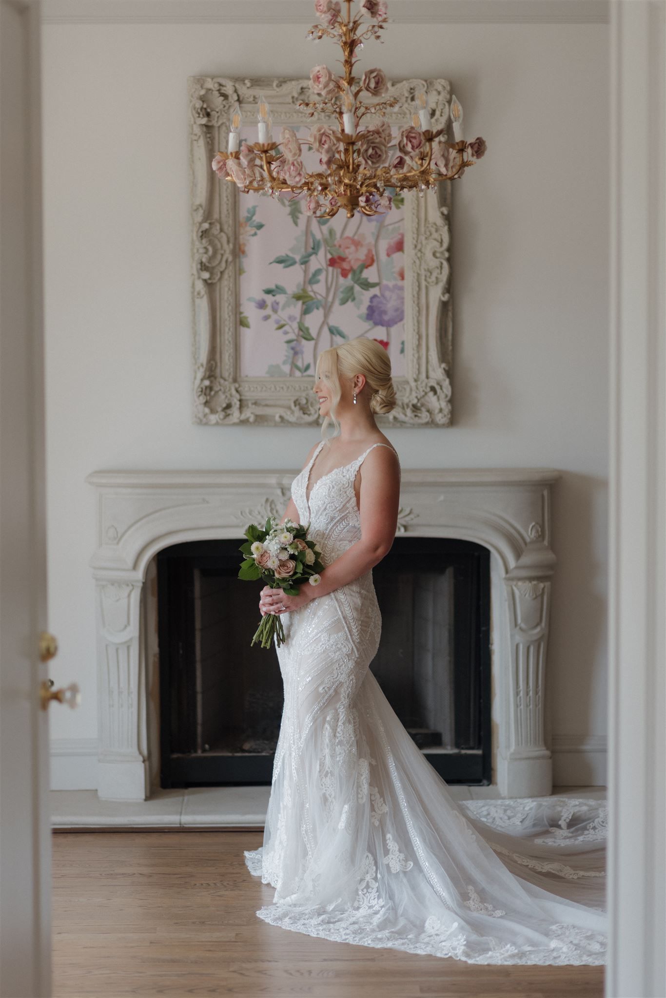 Bridal portrait with bouquet in front of ornate fireplace and floral artwork.