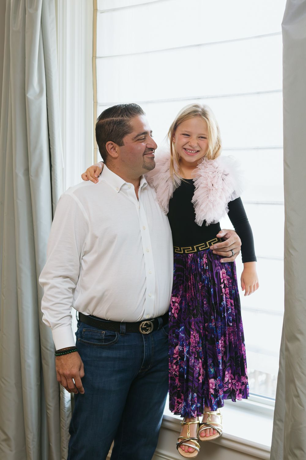 Dad and daughter candidly smiling by the suite window, photo by Paula Ortiz NYC Family Photographer