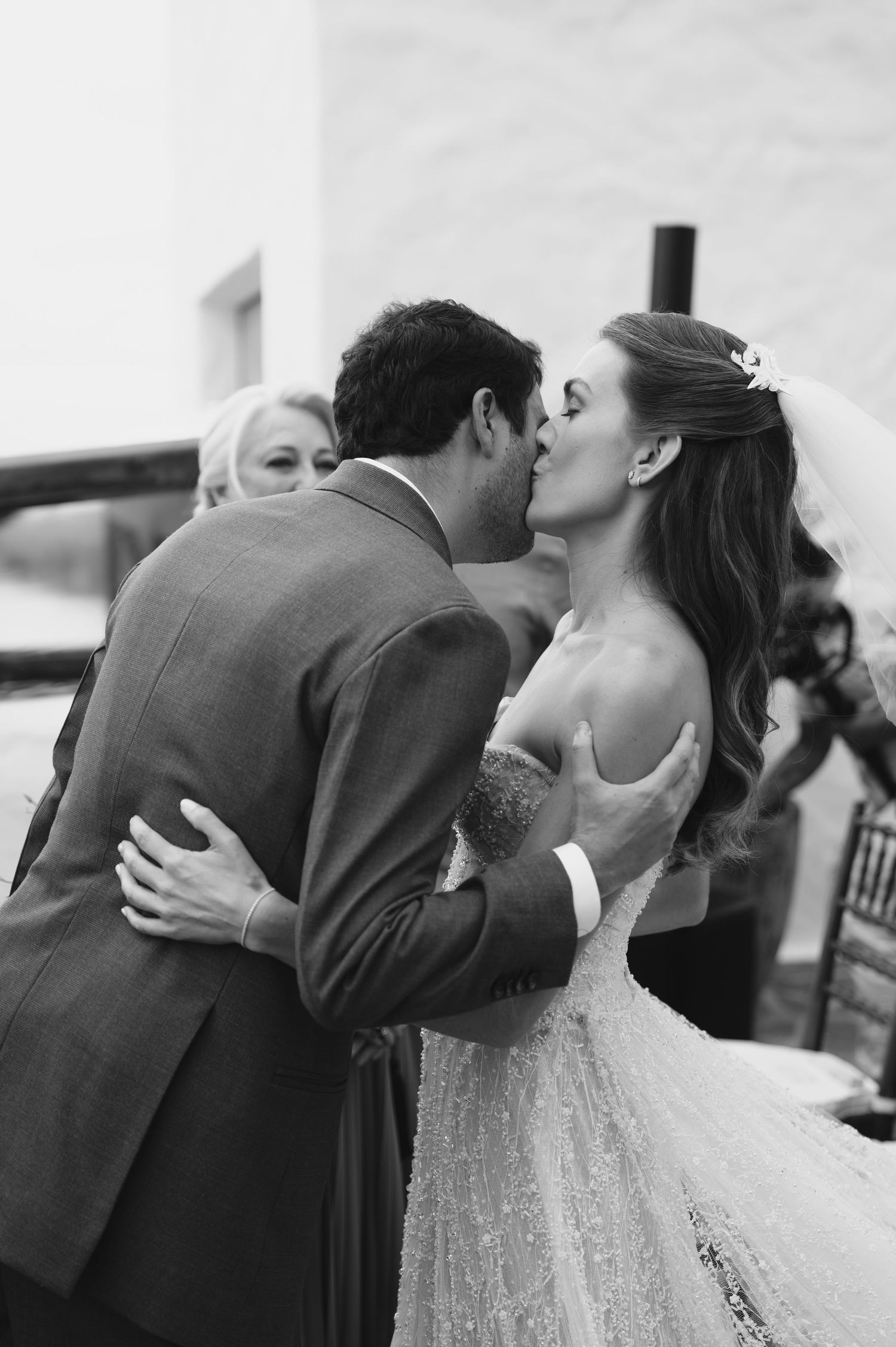 Black and white candid wedding kiss moment at outdoor ceremony.