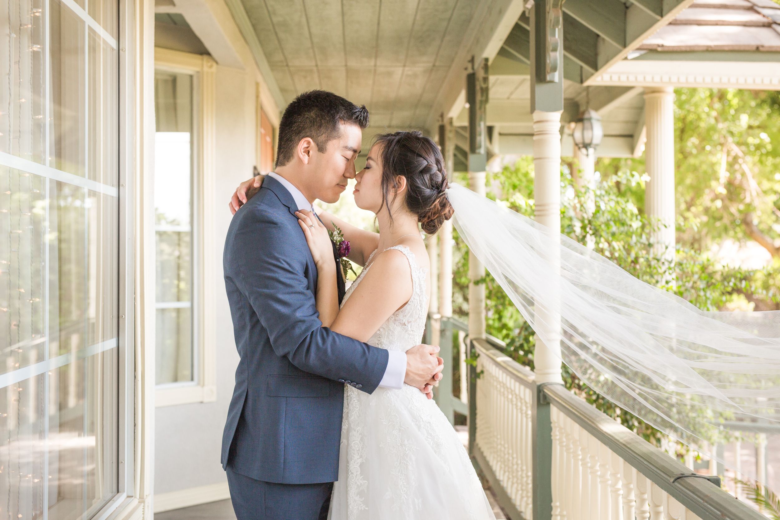A tender wedding moment captured on a covered porch with flowing veil details.