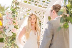 Wedding ceremony under a white arbor decorated with pink and white flowers.