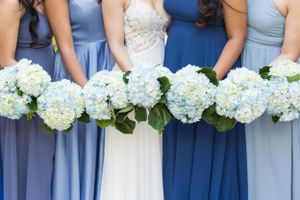 Row of blue and white hydrangea bouquets held against bridesmaid dresses in varying shades of blue.