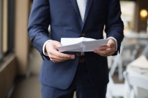 Close-up of hands holding wedding ceremony papers in navy suit jacket.