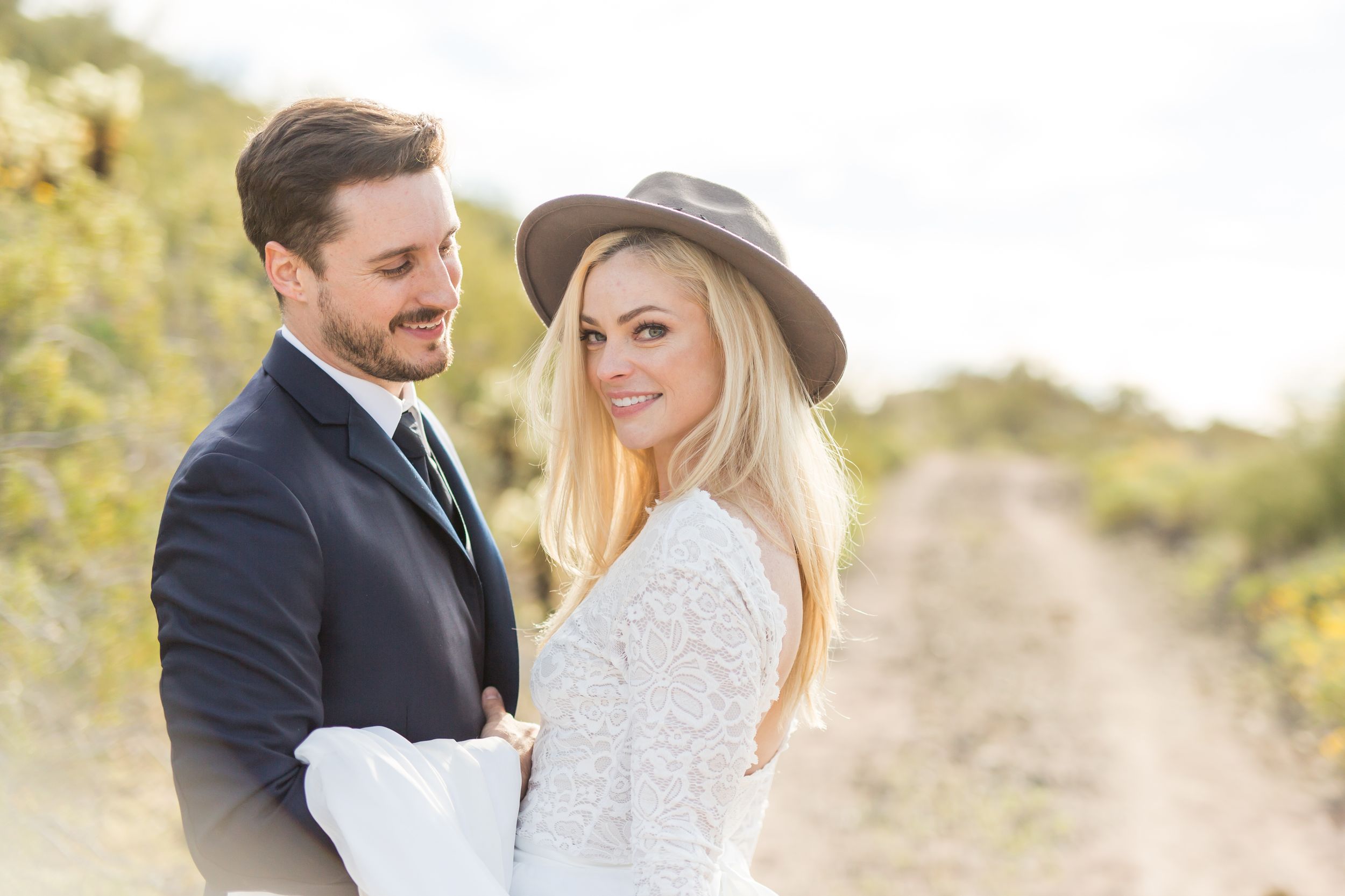 A romantic desert wedding portrait featuring elegant attire and a wide-brimmed hat.