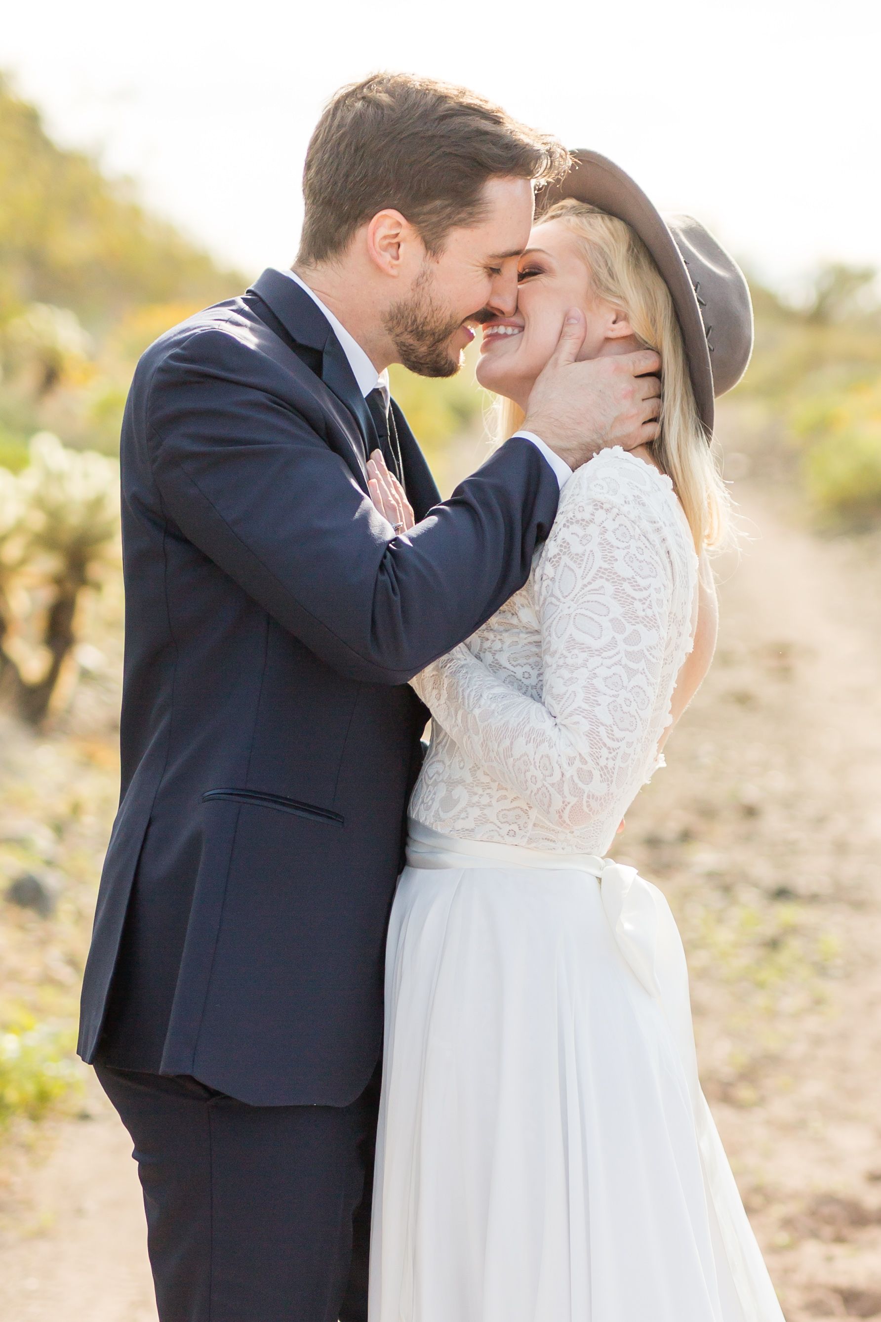 A romantic moment between newlyweds in formal attire against a desert backdrop.