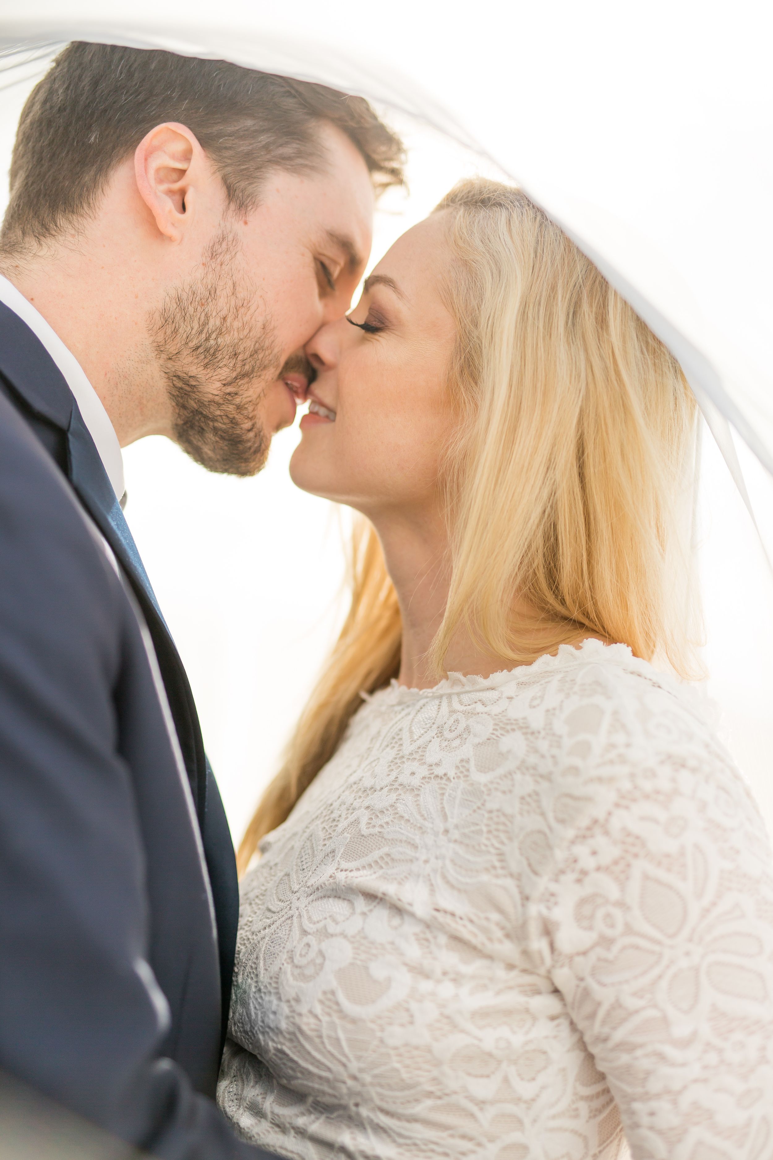 Romantic close-up portrait of newlyweds sharing a kiss under a delicate veil.