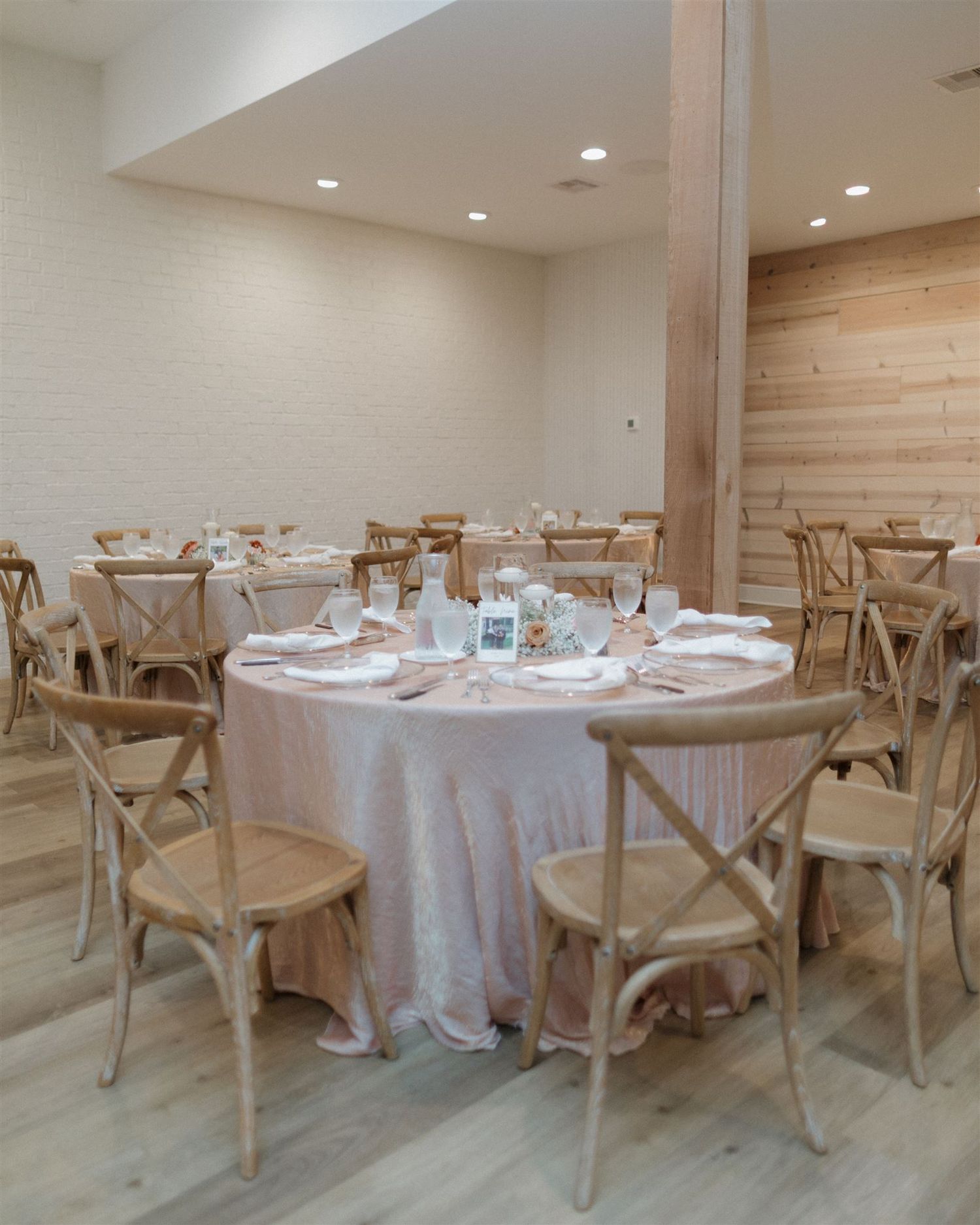 Modern wedding reception venue with round tables, white linens and wooden cross-back chairs.