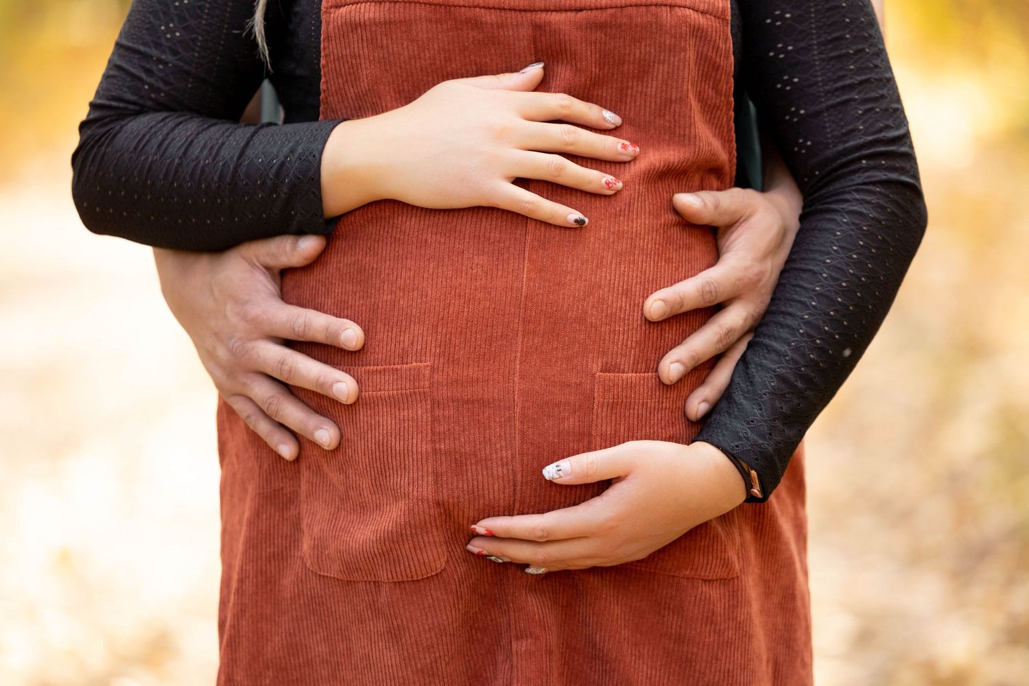 Girl in red jumper holding her stomach during a fall maternity session
