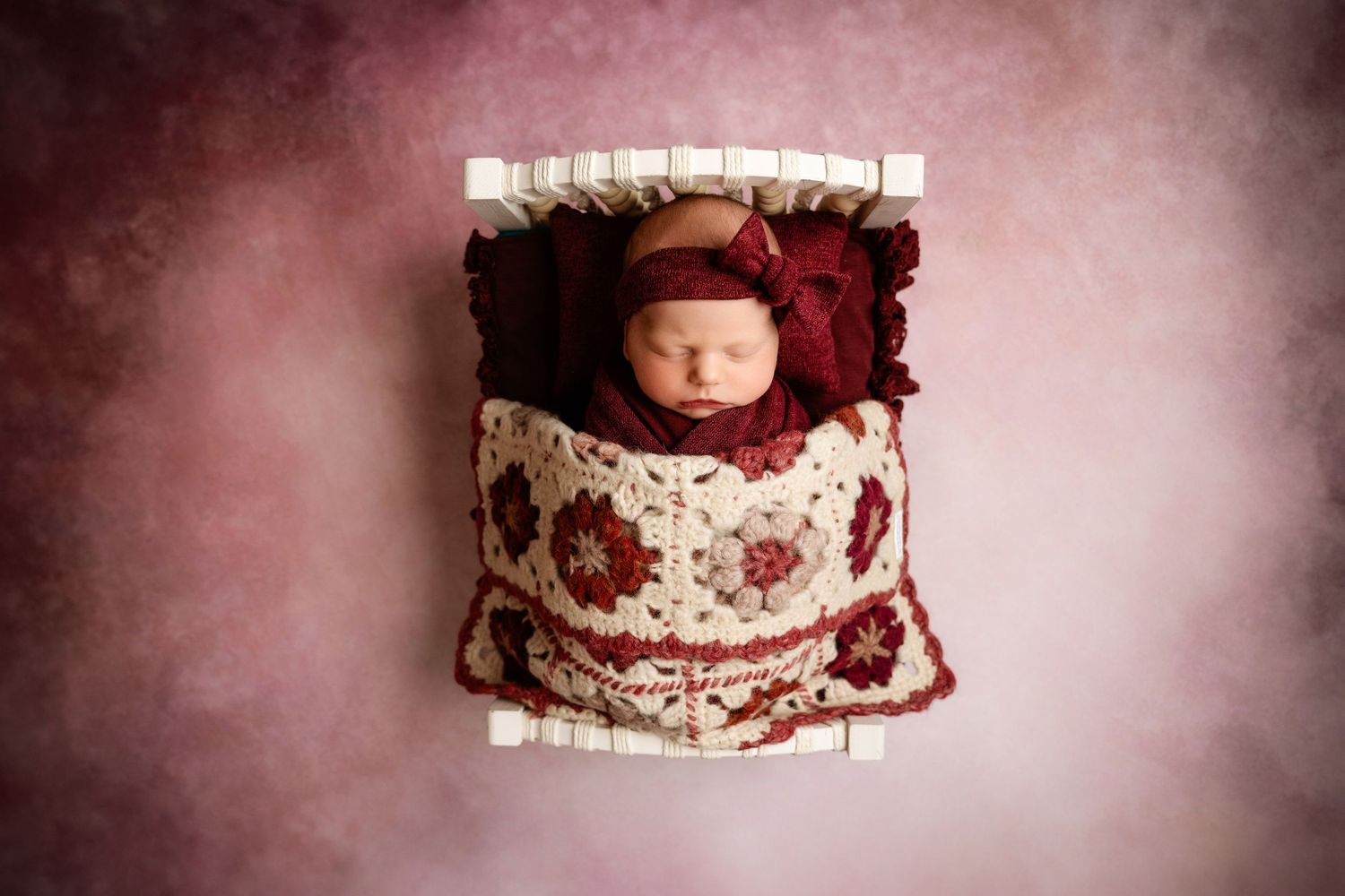 Newborn baby sleeping in a decorative pink and white bed with floral patterns.