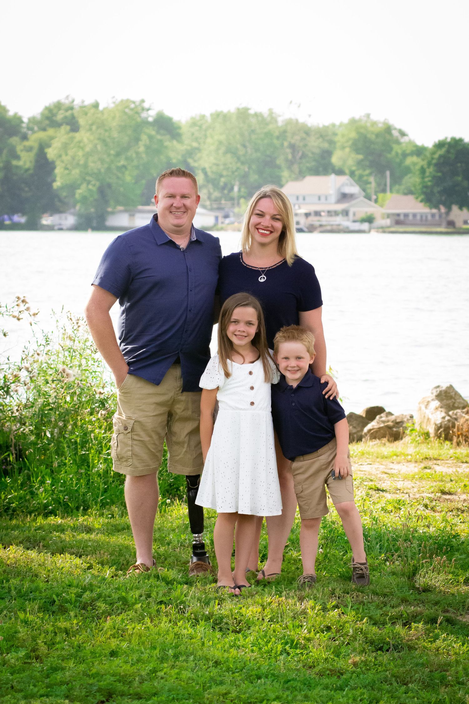 Family of four in navy and khaki posing by a lakeside on a warm summer evening.