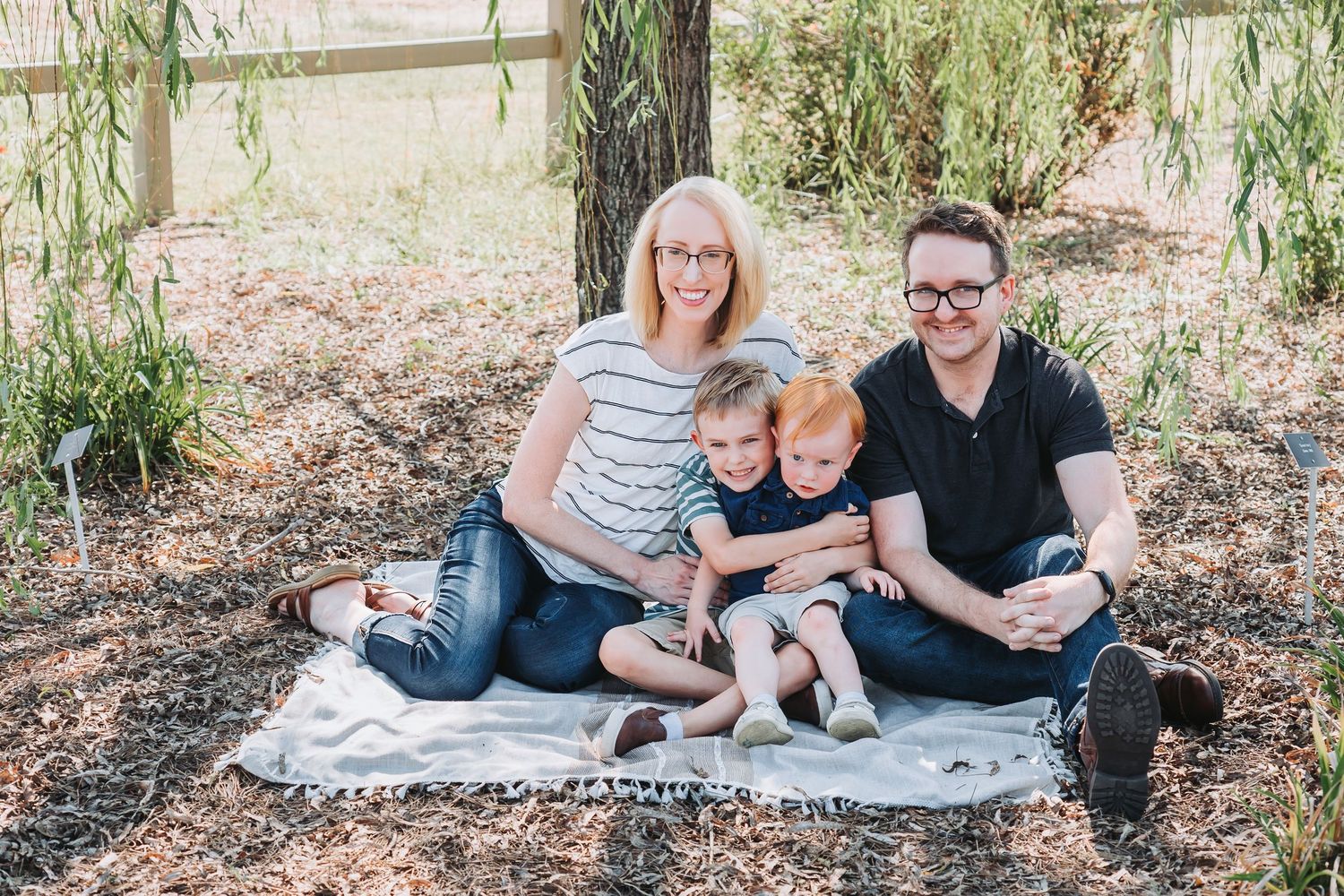 A family relaxes on a blanket during an outdoor photo session in a garden setting.
