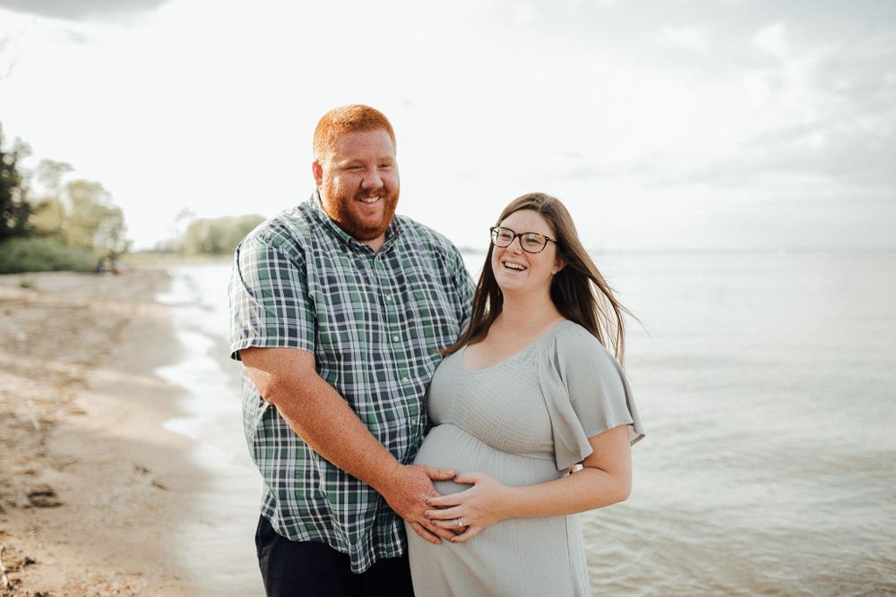A couple shares a tender moment during their maternity photoshoot on a beach at sunset.