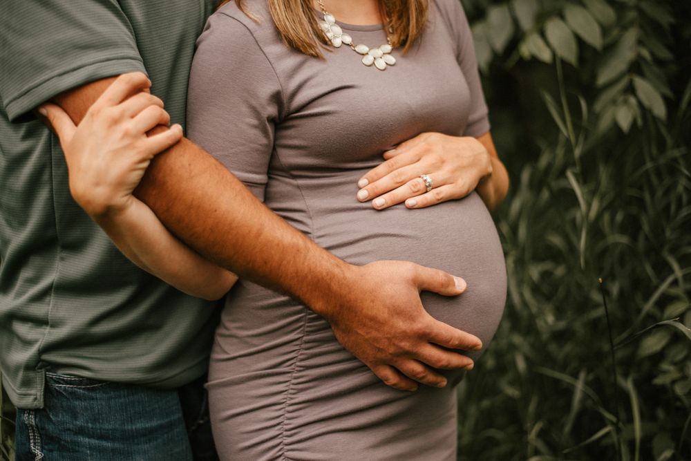 Intimate maternity moment captured with hands cradling a pregnant belly against lush greenery.