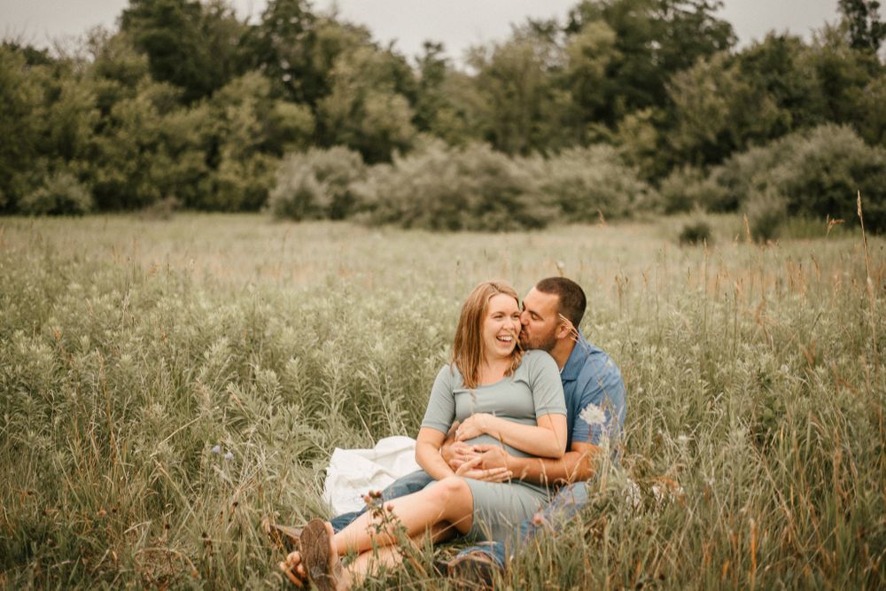 Couple sits together in a sunny meadow sharing an intimate moment.