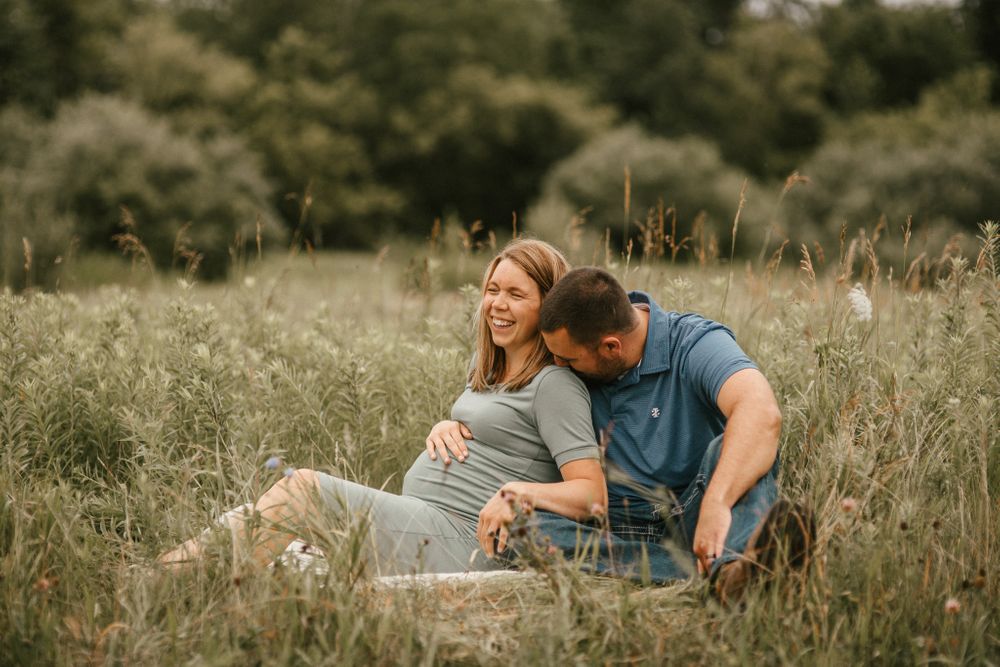 Couple lounging together on blanket in tall grass field during sunset.