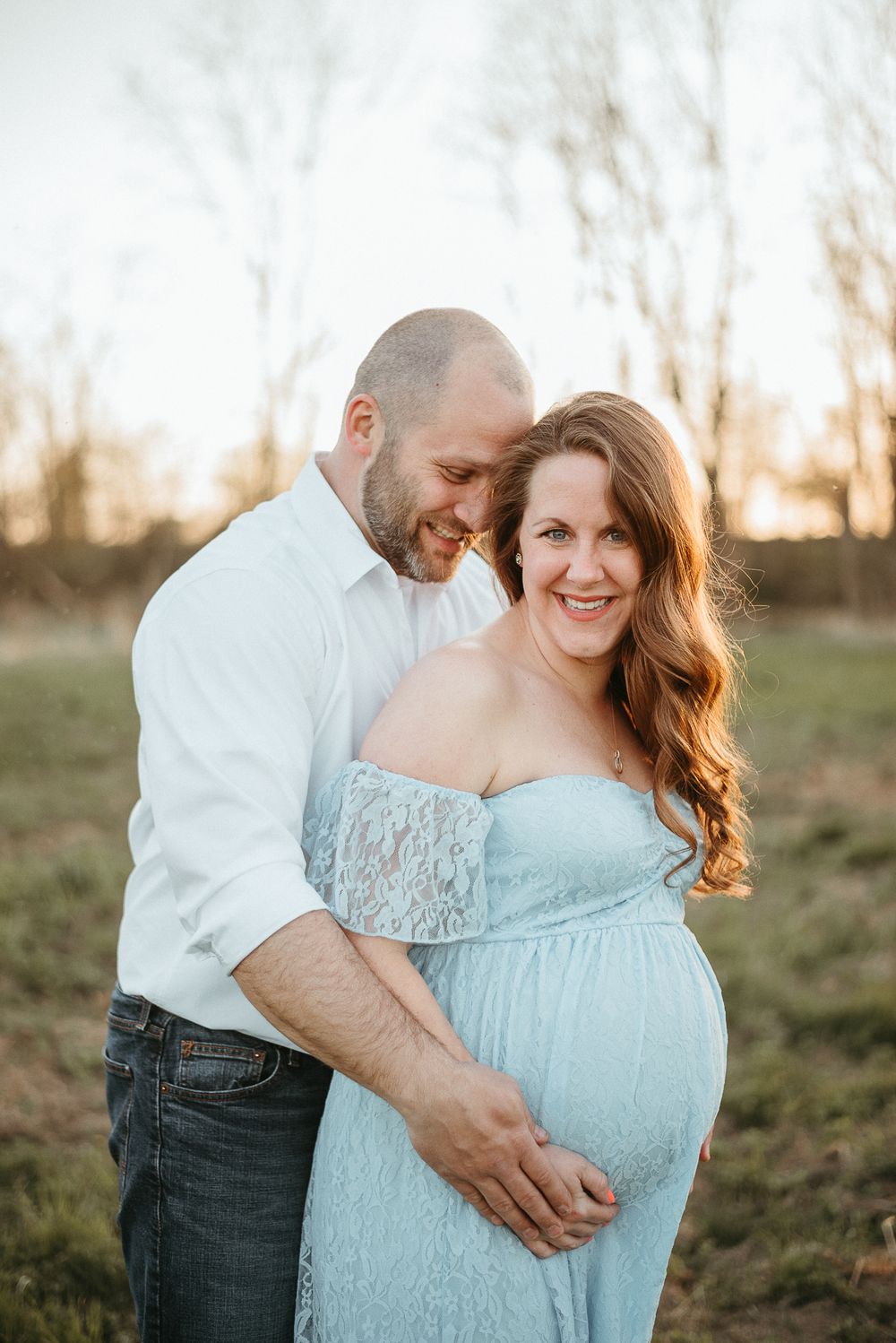 A romantic maternity portrait in a pale blue lace dress at sunset in a field.