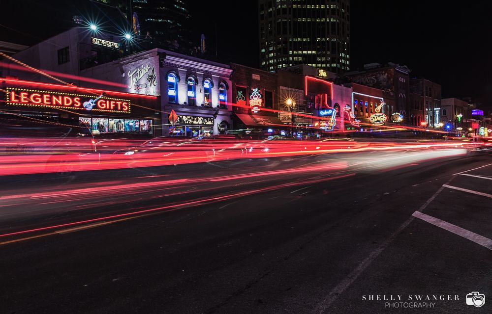 Long exposure of car light trails on Broadway Street in downtown Nashville at night.