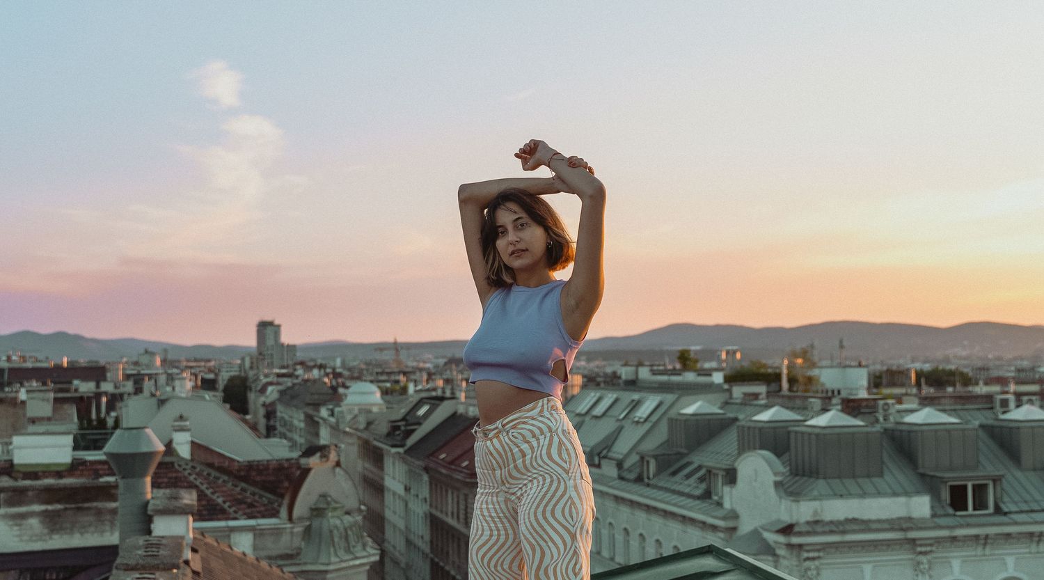 A silhouette poses against a sunset sky over a city rooftop.
