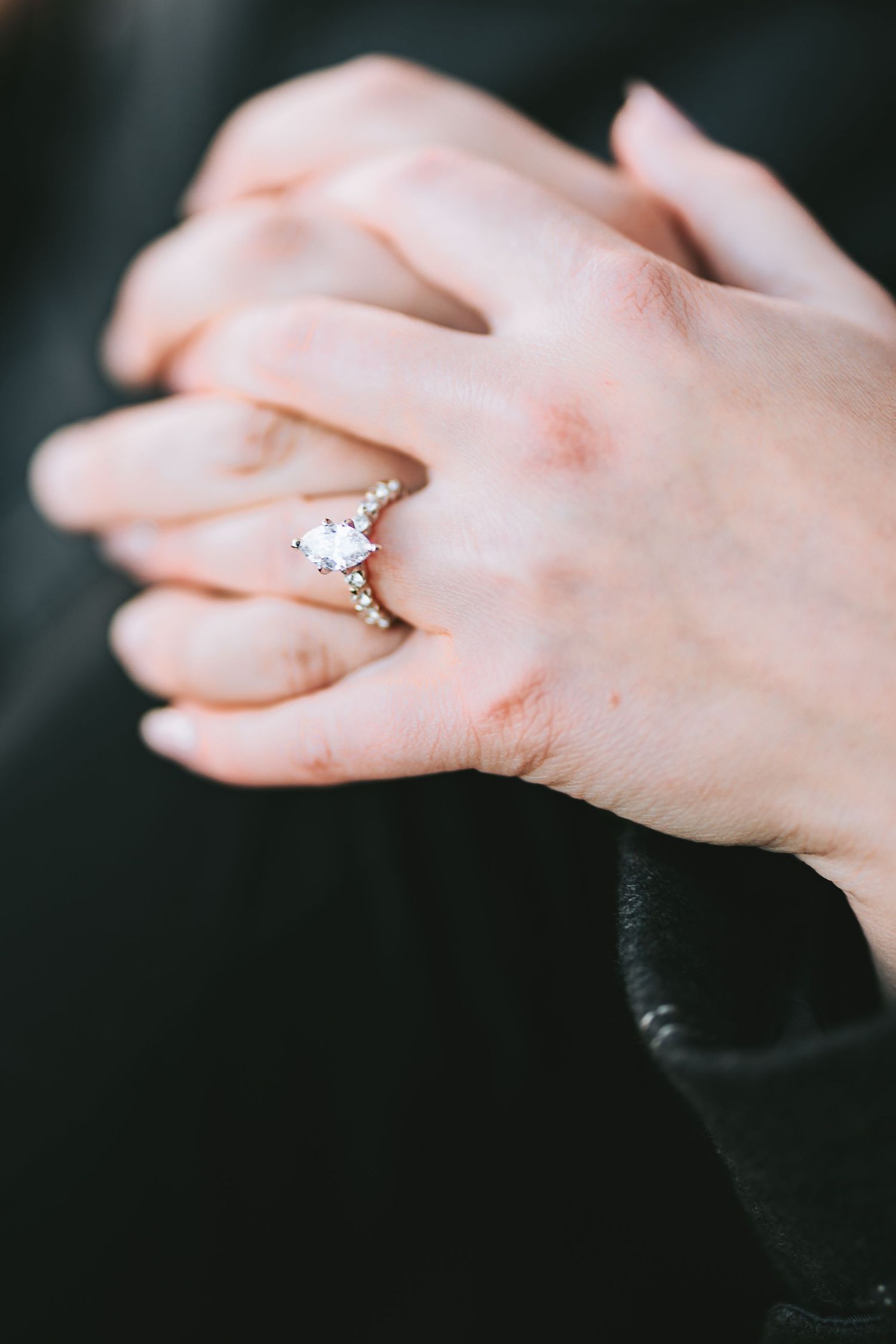 Close-up of an engagement ring on a hand with a black background.