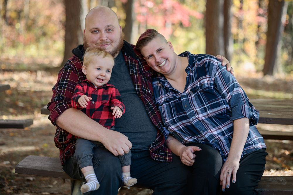 Family group poses together on picnic table during outdoor autumn photo session.