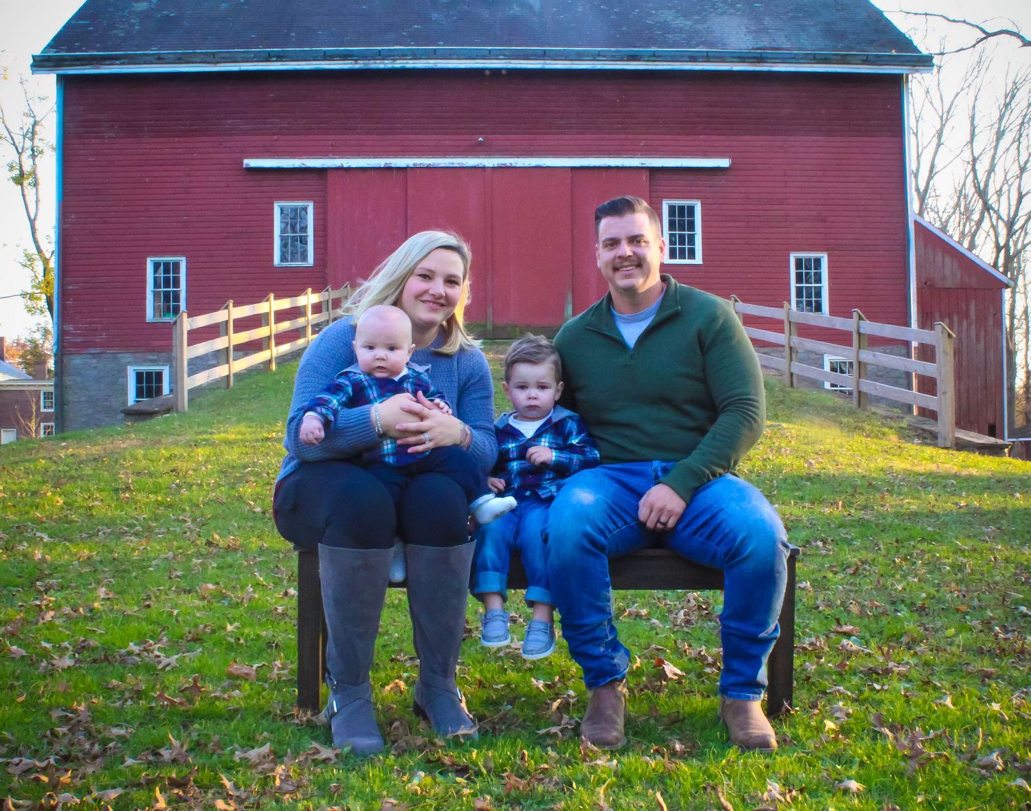 A group poses in front of a classic red barn with white trim on a grassy hillside.