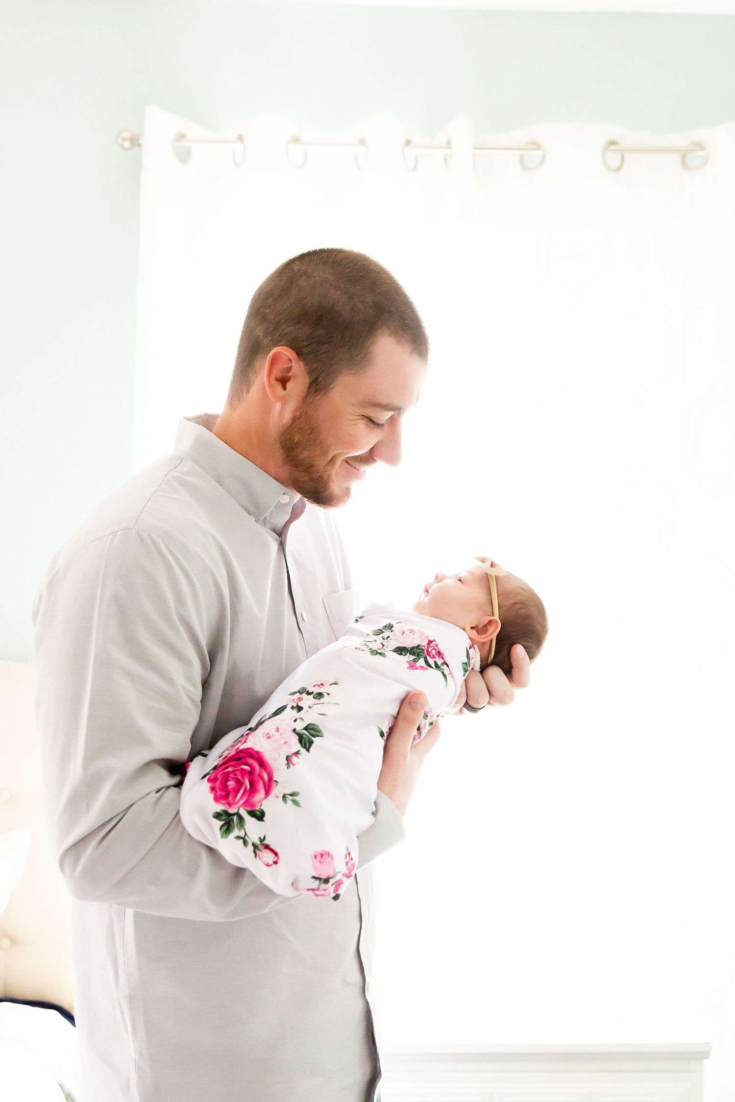Parent holding sleeping infant wearing floral outfit in bright white room.