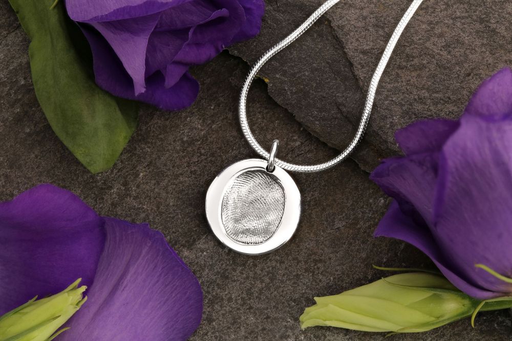 Silver fingerprint pendant necklace with purple iris flowers on dark stone background.