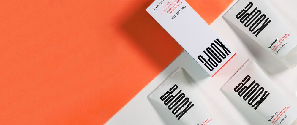 Minimalist white cosmetic product packaging against coral orange background.