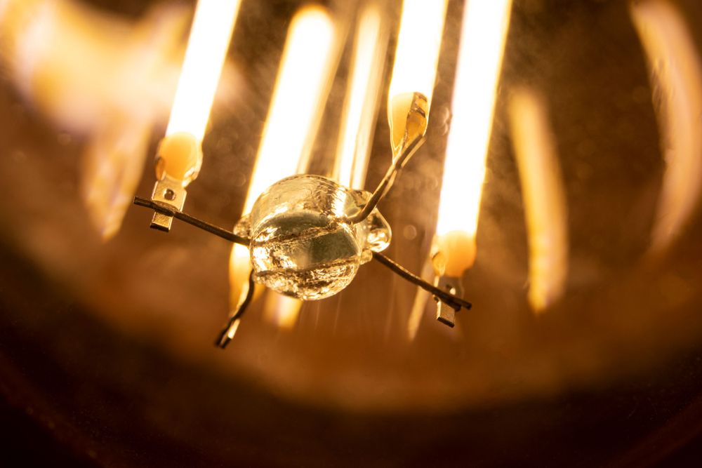 Closeup detail of glowing filaments inside a vintage light bulb with warm amber lighting.