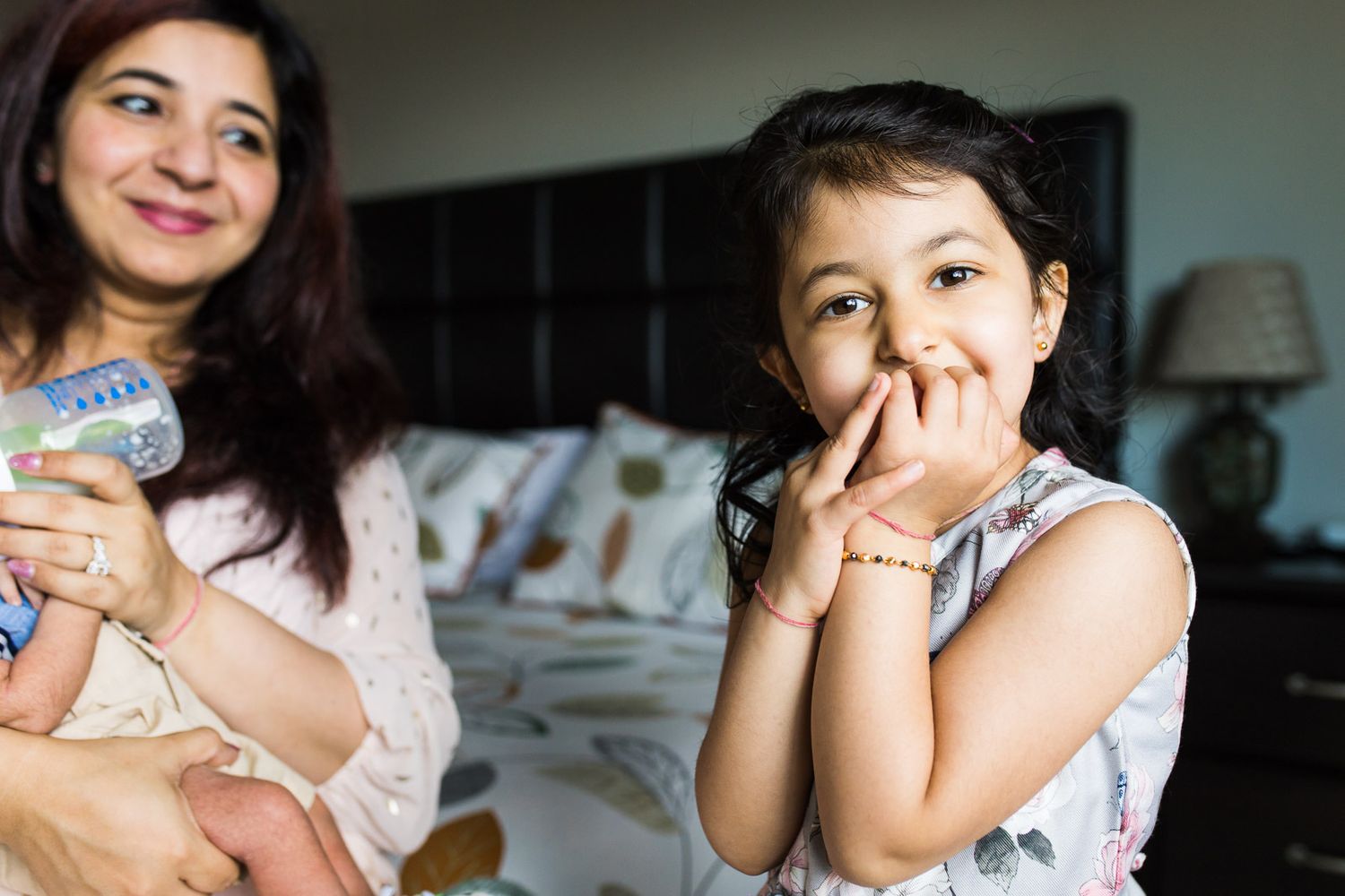Newborn photography captures a candid moment of sibling smiling while mom and newborn look on