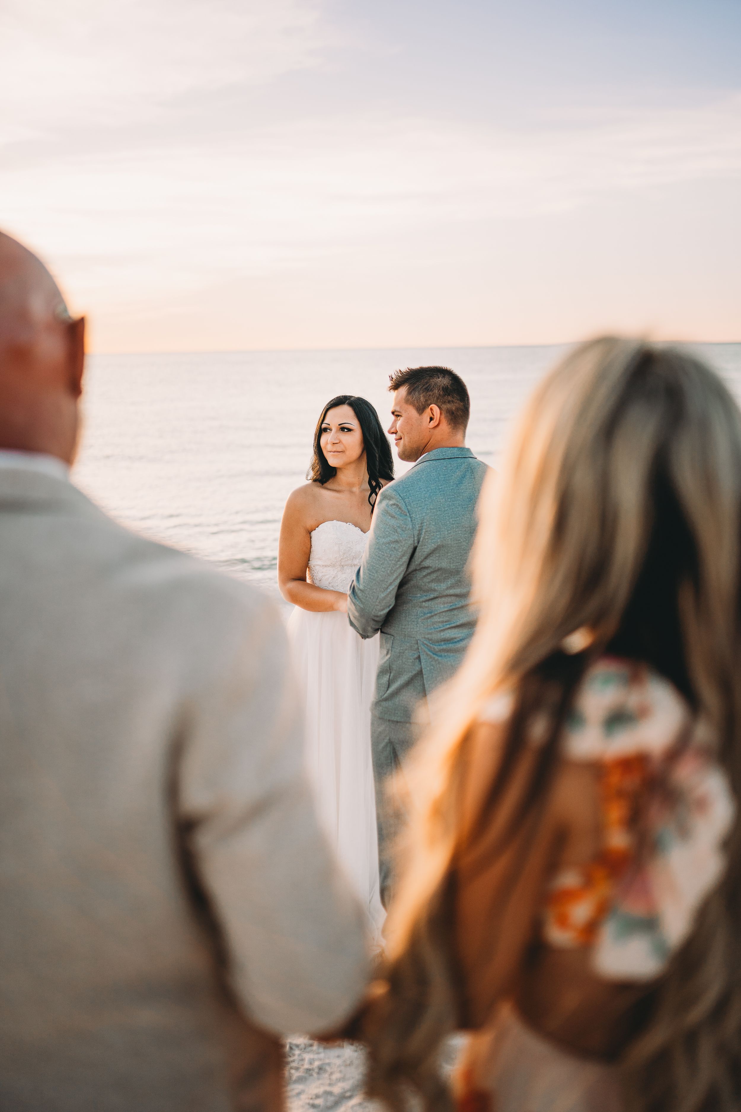 Beachside wedding ceremony at sunset with guests watching in foreground.