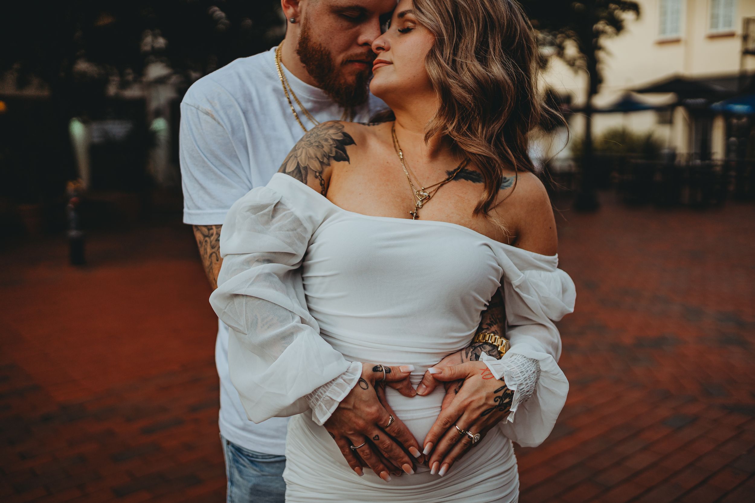 A romantic couple in white outfits forms a heart shape with their hands while embracing.