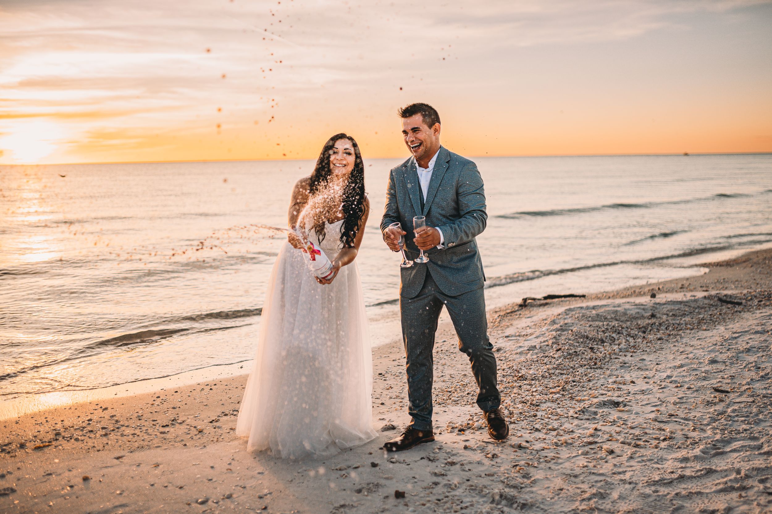 Wedding couple shares joyful moment on sandy beach during golden hour sunset.