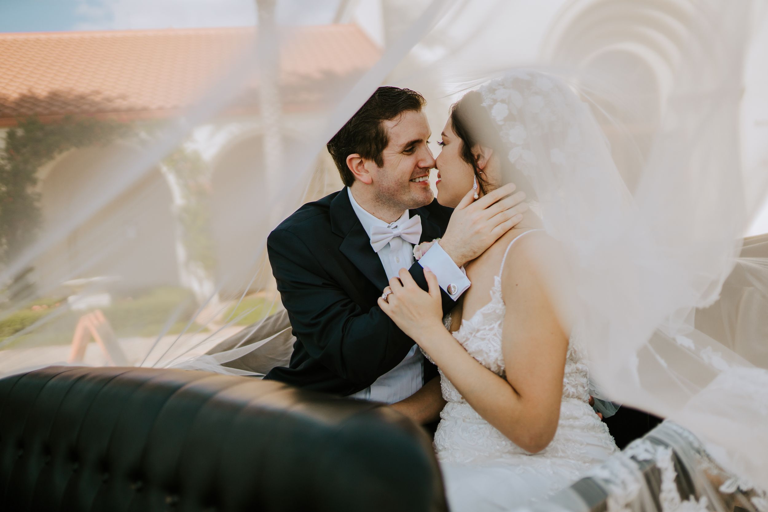 Wedding couple shares tender moment with flowing veil indoors.