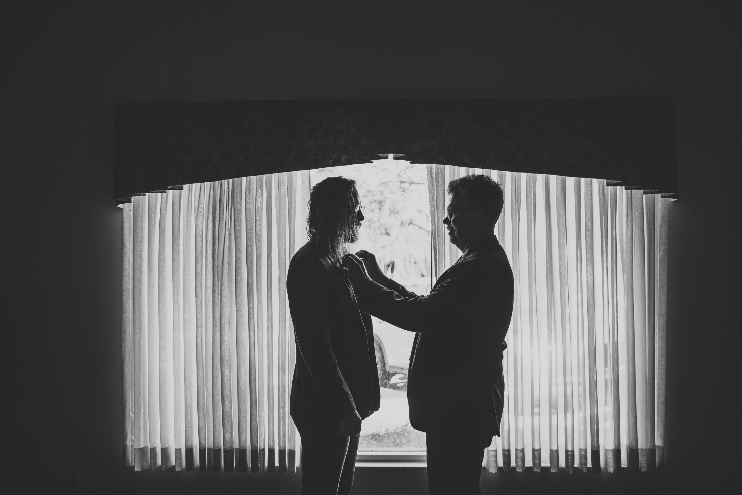 Silhouetted figures in intimate moment against backlit sheer curtains.