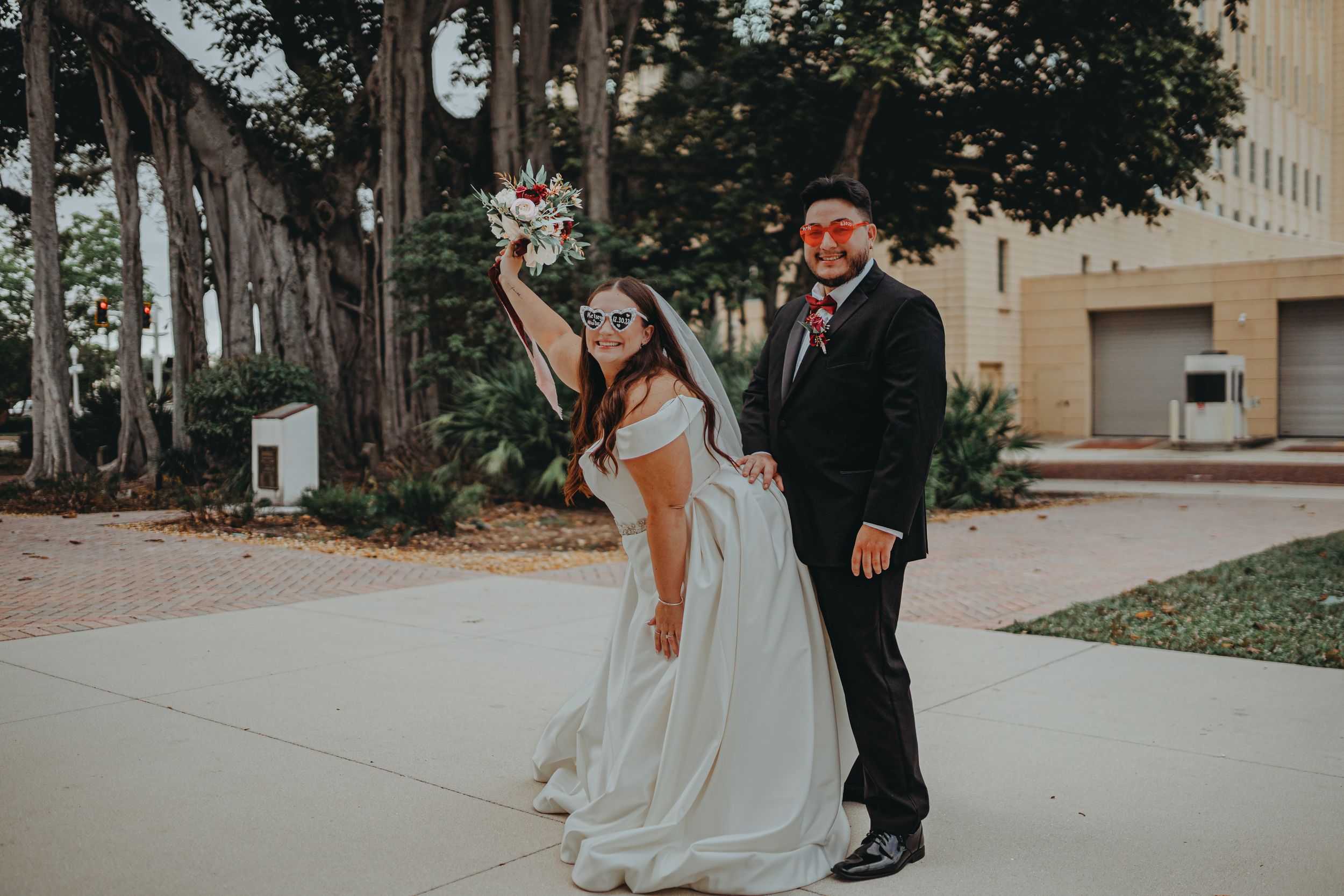 Newlywed couple poses playfully outdoors with bride in white dress and groom in black suit.
