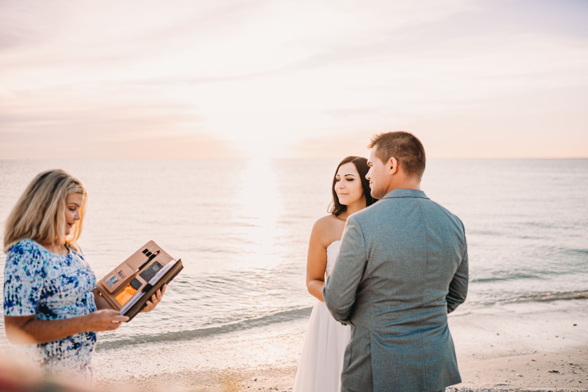 Beach wedding ceremony with officiant reading from book during sunset.